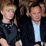 Kobieta w czarnej sukni z ozdobnym kołnierzem i mężczyzna w garniturze siedzą obok siebie.