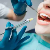 Dentysta podaje znieczulenie. Czy znieczulenie u dentysty boli? Pacjentka ma otwarte usta, a w nich widać igłę strzykawki.