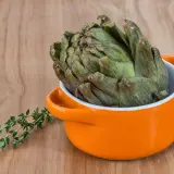 Un gros artichaut vert prêt pour la cuisson Cookeo, avec une branche de thym frais à côté.