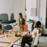 Zespół dyskutuje przy stole, czy umowa zlecenie przedłuża się automatycznie. Kobieta prezentuje coś na laptopie.