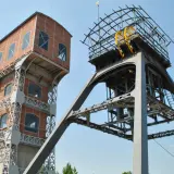 Dwie wieże kopalniane, jedna ceglana, druga metalowa z kołem, tworzą futurystyczny grawitacyjny magazyn energii.