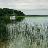 Żaglówka na jeziorze, w oddali las i zabudowania. Odległość do Mikołajek Giżycko.