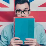 Studente con quaderni davanti al volto, sullo sfondo la Union Jack. Chissà se impara come si dice "venerdì" in inglese.