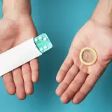Deux mains ouvertes présentent une plaquette de pilules contraceptives et un préservatif, symbolisant les options de contraception hormonale masculine.