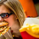 Dziewczyna w okularach je pysznego mcmuffin wieprzowy z jajkiem. Obok frytki.