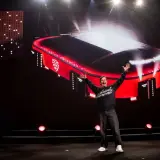 En man med armarna uppsträckta jublar framför en storbildsskärm som visar en röd arena med texten "Strawberry Arena".