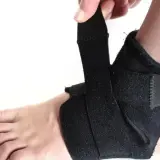 Dłoń zapina czarny stabilizator na kostce. Zapewnia wsparcie i ochronę podczas aktywności.