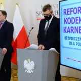 Konferencja prasowa dotycząca reformy kodeksu karnego. Mówcy przy mównicach z godłem Polski, na ekranie hasło "Bezpieczeństwo dla Polaków" i symbole sprawiedliwości.