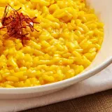 Aksamitne risotto alla milanese, złociste od szafranu, podane w białej misce, ozdobione nitkami szafranu.