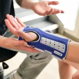 Ein Arzt erklärt, wie ein Handgelenk-Korsett bei einem Wirbelbruch auch nachts getragen werden sollte, um die Heilung zu unterstützen.