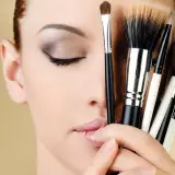Mujer con ojos cerrados y varios pinceles de maquillaje, inspirando ideas de maquillaje.