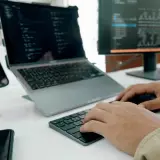 Programista pracuje nad nowym oprogramowaniem użytkowym, pisząc kod na laptopie i monitorze.