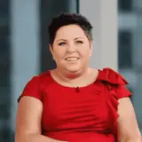 Uśmiechnięta Dorota Wellman w czerwonej sukience. Jej wiek nie jest widoczny, ale emanuje pewnością siebie.