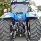 Blauer Traktor mit großen Reifen. An der Seite sind rot-weiße Warnschilder mit Beleuchtung angebracht.