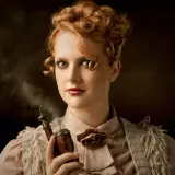 Artystyczna fotografia: rudowłosa kobieta w stylizacji retro z fajką w dłoni, z której unosi się dym.