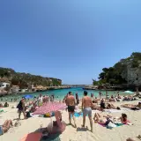Słoneczna pogoda na Majorce, plaża pełna ludzi kąpiących się i opalających.