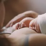 Delikatne dłonie noworodka obejmujące pierś podczas karmienia. Ulewanie u noworodka to częsty widok, ale ten moment to czysta bliskość.