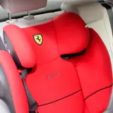 Czerwony fotelik samochodowy Cybex z logo Ferrari, zamontowany za pomocą pasa bezpieczeństwa. Instrukcja jak zamontować fotelik samochodowy.