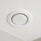 Biały, okrągły anemostat wywiewny zamontowany na białym suficie.