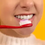 Dziecko przygotowuje się do fluoryzacji zębów, nakładając pastę na czerwoną szczoteczkę.