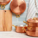 Utensilios de cobre apilados y colgados, junto a una tabla de cortar. Aprende como limpiar cobre para que brillen así.
