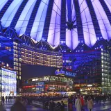 Nocny widok na Sony Center w Berlinie, z oświetlonym dachem i fasadami budynków, pełen ludzi spacerujących po placu.