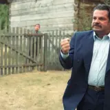 Mężczyzna w garniturze, jakby z filmu "To ja, złodziej", pokazuje pięść. Za nim przez płot wyglądają inni.
