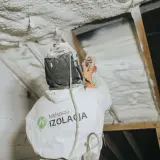 Pracownik w kombinezonie natryskuje twardą piankę poliuretanową na poddasze, tworząc skuteczną izolację.