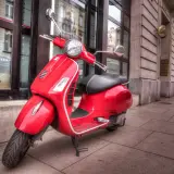 Czerwony skuter Vespa, idealny do zdobycia **prawo jazdy AM**, stoi na chodniku przed budynkiem.