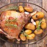 Gigot d'agneau rôti, doré et savoureux, accompagné de pommes de terre grenaille et d'ail, prêt pour la cuisson.