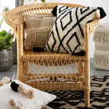 A rattan chair with decorative pillows and a fringed pouf, showcasing various types of fancy chairs and bohemian decor.
