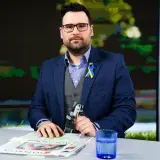 Michał Sznajder, w garniturze z niebiesko-żółtą wstążką, przygotowuje się do wywiadu. Jego życiorys to historia dziennikarza.