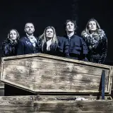Aktorzy Teatru Pantomimy Wrocław w strojach z epoki stoją nad otwartą trumną, z której wystaje ręka.