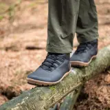Black, low-profile shoes with tan soles, perfect as shoes to wear in winter besides boots, balance on a mossy log in a forest.