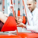 Fizjoterapeuta wspiera pacjenta podczas terapii wiszącej, która pomaga w leczeniu problemów z kręgosłupem.