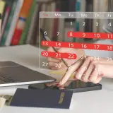 Planowanie urlopu: 26 dni wolnego do wykorzystania. Na biurku laptop, paszport, pieniądze i kalendarz.