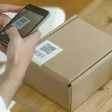 Ręce skanują kod QR na paczce, przygotowując ją do wysyłki w ramach dropshippingu.