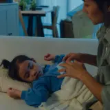 Mamma accarezza dolcemente il suo bambino che dorme sul divano, uno dei tanti bambini che si svegliano di notte.