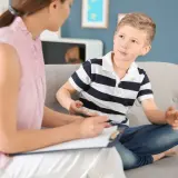 Psycholog rozmawia z chłopcem siedzącym na kanapie.