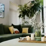 Stolik z świecami i gałązką kwitnącej wiśni, zielona kanapa w tle. Aranżacja zgodna z zasadami feng shui, wprowadzająca harmonię.