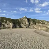 Plage de Patti, Sicile. Un château domine la colline rocheuse surplombant la mer calme et la plage de sable.