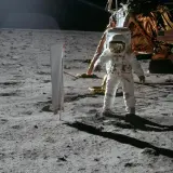 Astronaut na Księżycu podczas misji Apollo, obok lądownika. W tle amerykańska flaga.