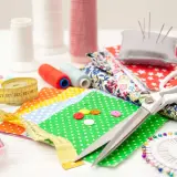 A collection of 10 sewing tools: scissors, measuring tape, spools of thread, needles, buttons, and fabric scraps, ready for a creative project.