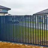 Nowoczesne ogrodzenia grzebieniowe w ciemnym kolorze, chroniące posesję z domami w tle.