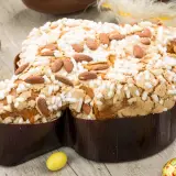 Colomba pasquale ricetta: dolce soffice con mandorle e glassa croccante, circondata da uova di cioccolato e coniglietti.