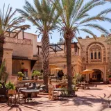 Sonniger Innenhof mit Palmen und traditioneller Architektur in der Agadir Altstadt. Tische und Stühle laden zum Verweilen ein.