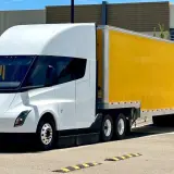 Biała ciężarówka Tesla Semi z żółtą naczepą DHL stoi na parkingu.