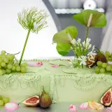 Elegancki tort ślubny w pastelowej zieleni, ozdobiony winogronami, figami i białymi kwiatami.