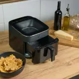 Chrupiące chipsy z airfryera w misce obok urządzenia. Na desce ser, oliwa, wino i kieliszki.