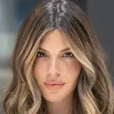 Mujer con pelo castaño con canas y mechas rubias, con ondas suaves y raya en medio.